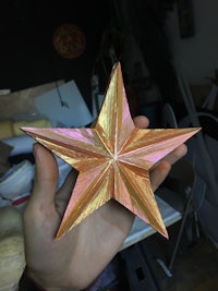 a person holding up a gold and pink origami star